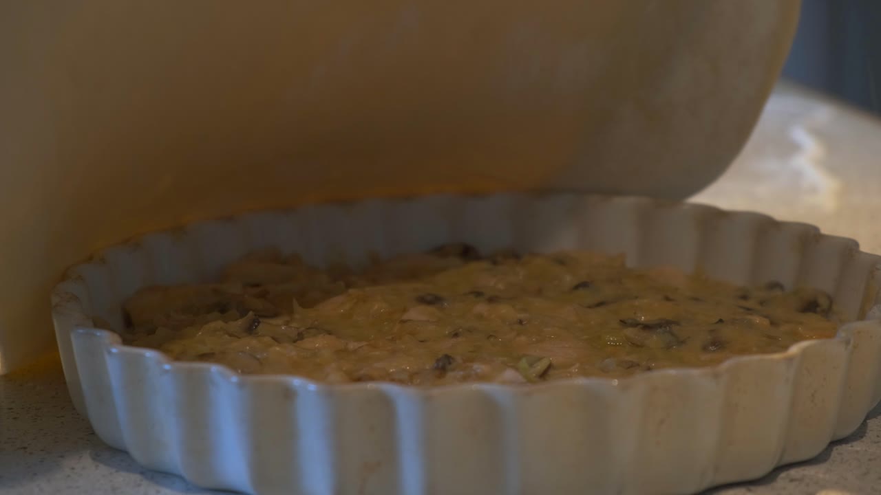 Close up of the golden filling of mushroom, chicken and onions sits in the pie tray as the cook gently places the dough over it and seals the edges with care.
