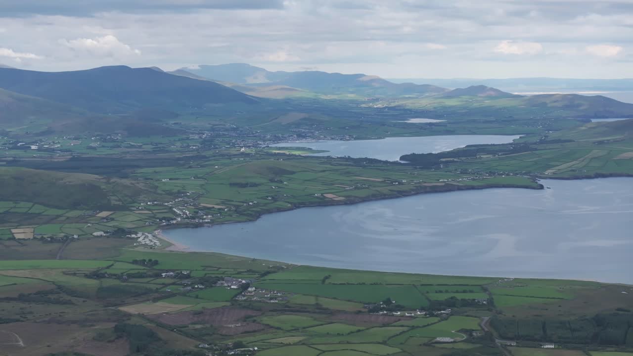 Impresionantes imágenes de dron que capturan el exuberante paisaje verde de la Península de Dingle, con la Bahía de Ventry y montañas distantes bajo un cielo irlandés nublado.