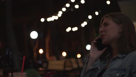 una mujer hablando por teléfono en un café nocturno.
