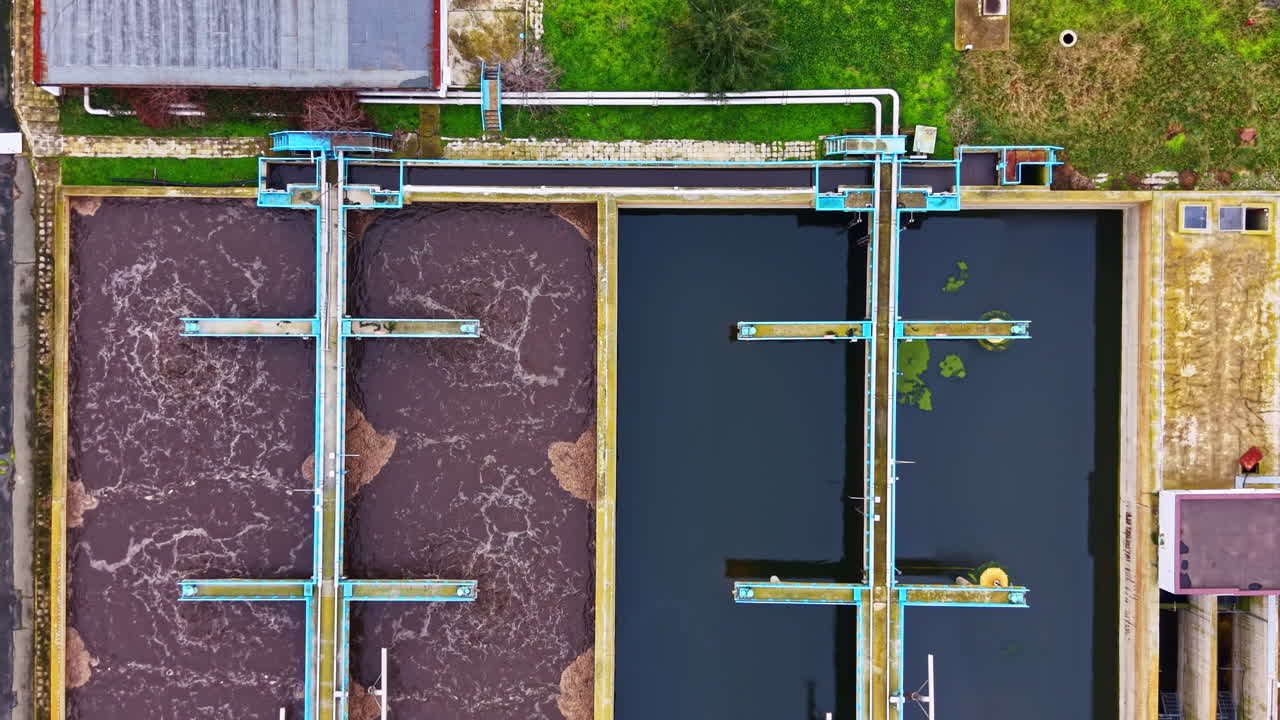 Water treatment facility with large tanks seen from above during daytime in an urban area next to a road