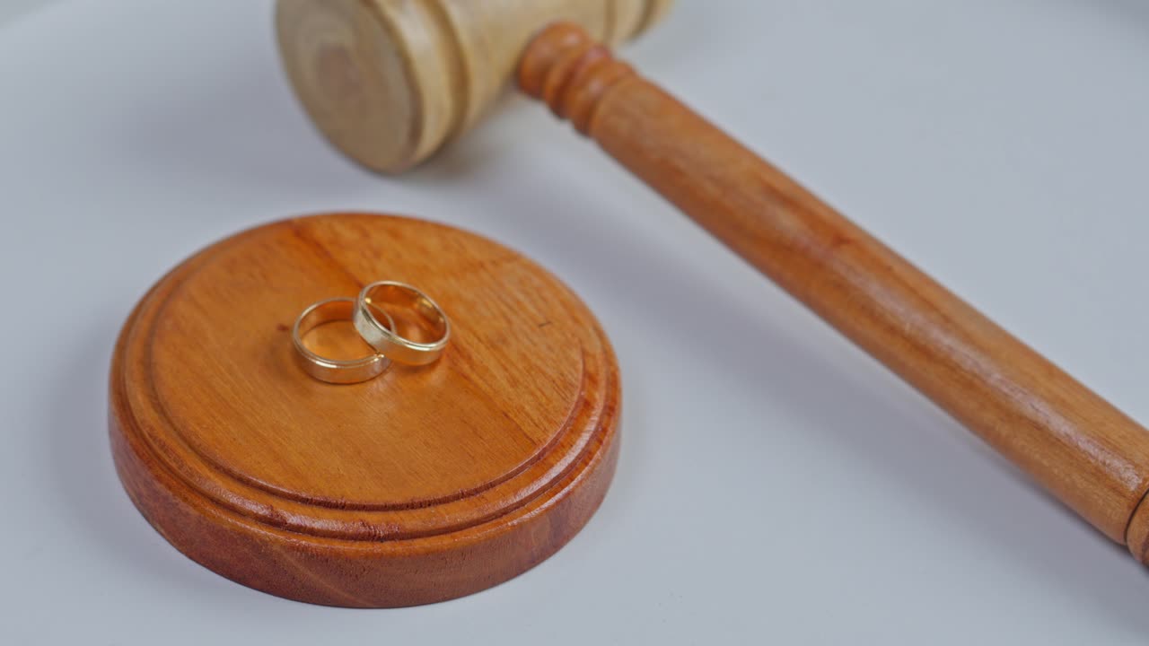 Legal concept of divorce featuring wedding rings and wooden gavel on white background
