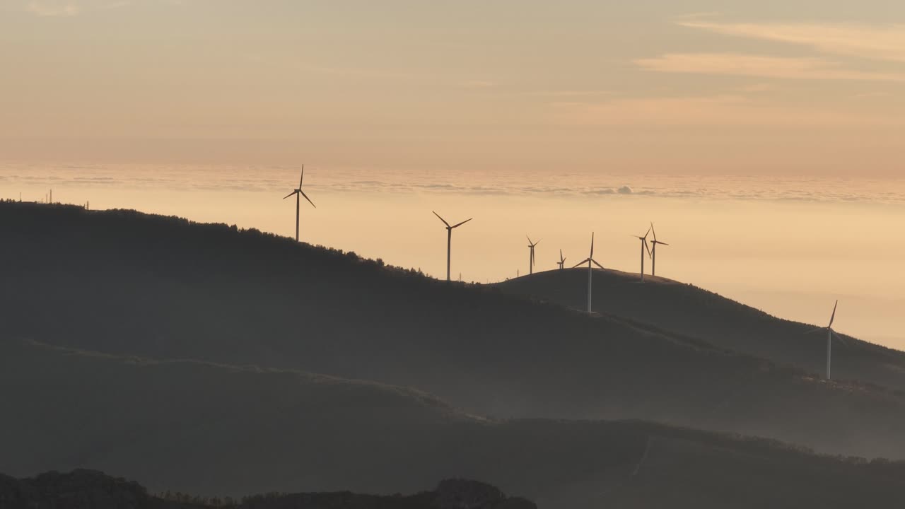 Rotating wind turbines on hills in Portugal at sunset.