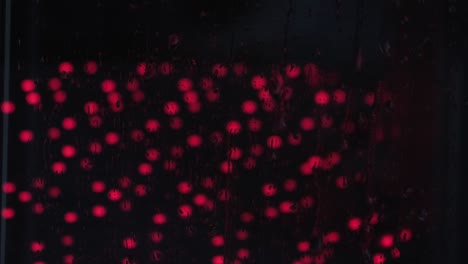 gotas de lluvia en el vidrio de la ventana primer plano con luz roja. reflejo de la luz nocturna en vidrio húmedo. textura de fondo de gotas