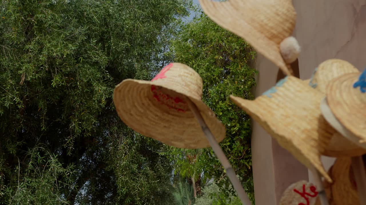 Close-up view of straw hats hanging on bamboo sticks inside a Moroccan vase, highlighting textures and classic geometric architecture in Marrakesh, Morocco