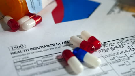 prescription drug bottle and pills spilling onto a patient health insurance claim form