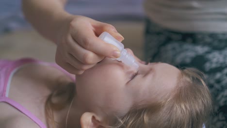 mommy gives eye drops to crying girl on soft bed closeup