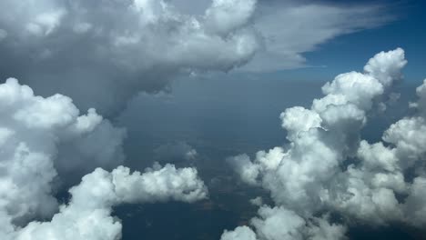 immersive pilot’s perspective, pov fpv in a real time flight through a blue sky with a huge storm cloud on the left hand side and some beautiful cottony clouds bellow