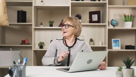 older woman in glasses orders food delivery online while sitting behind her laptop, and the courier swiftly delivers it, leaving the woman impressed and smiling