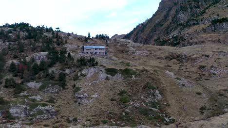 Le-Refuge-d'Espingo-chalet-at-Lac-d'Espingo-lake-in-Haute-Garonne,-Pyrénées,-France,-Aerial-orbit-around-approach-shot