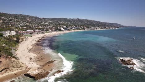 Flying-over-the-beach,-Pacific-Ocean,-rocks,-and-cliffs-towards-Main-Beach-in-Laguna-Ca