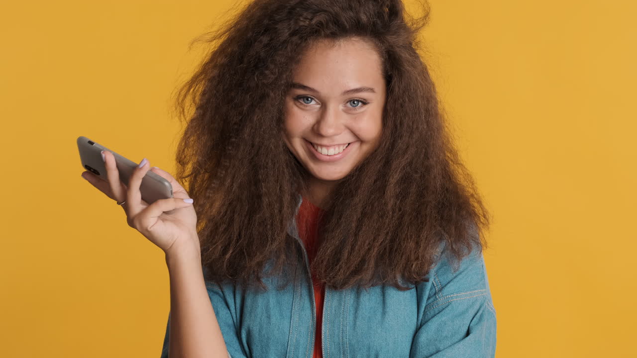 Caucasian curly haired woman using smartphone and smiling to camara.