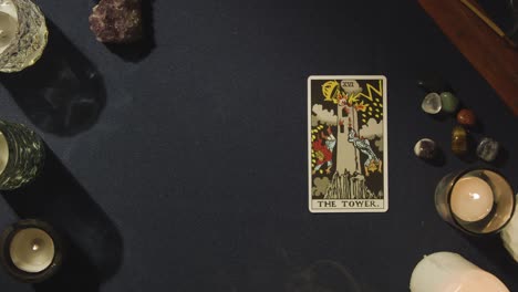 toma aérea de una persona que da una lectura de cartas del tarot con la carta de la torre acostada en la mesa