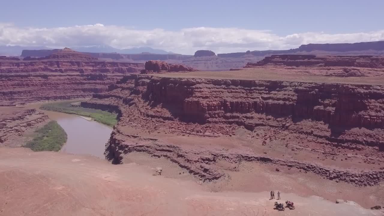 Vista di un canyon rosso roccioso sul fiume con due motociclisti in piedi sul bordo, ripresa a rivelazione da drone