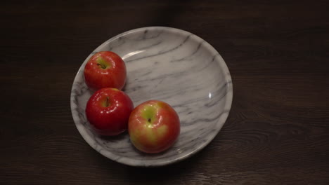 Closeup-of-woman-removing-red-apples-from-a-white-marble-bowl