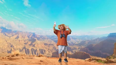 asian boy with a hat and binoculars waving hand having video call on smartphone while traveling at the top of mountain. boy researcher examines something, travel adventure, full body
