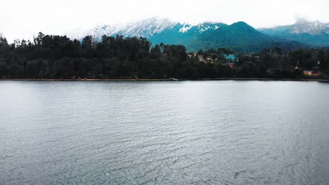 Luftaufnahme-Beim-Anflug-Auf-Einen-Kristallklaren-Und-Ruhigen-See-Im-Argentinischen-Patagonien,-Umgeben-Von-Bergen,-Deren-Gipfel-Von-Schnee-Und-Wolken-Bedeckt-Sind