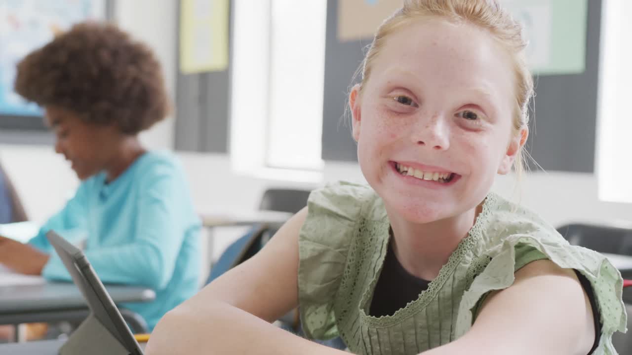 Ritratto video di scolaretta caucasica sorridente, seduta al banco, che usa un tablet in classe, con spazio per il testo.