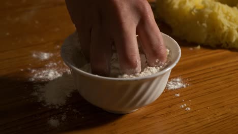 4k close up slow motion shot taking a handful of white flour from a white ceramic bowl on a wooden table