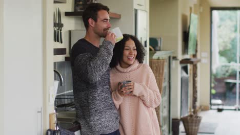 Happy-diverse-couple-talking-and-drinking-coffee-in-kitchen