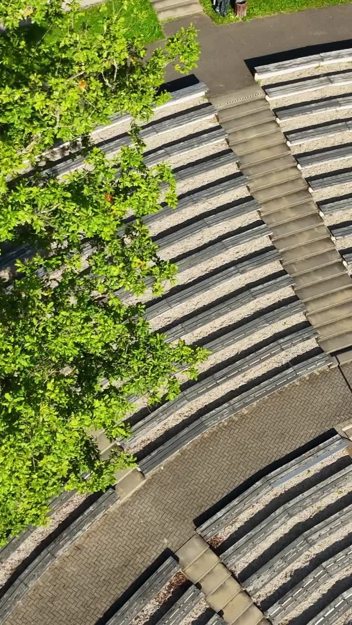 Sauleskalns open air theater nestled among lush greenery, revealing curved seating rows and distinctive architectural layout in Talsi, Latvia from above, vertical drone close up orbiting