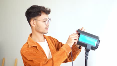 asian male photographer adjusting barndoors on studio light, fine tuning the direction and spread of the light source