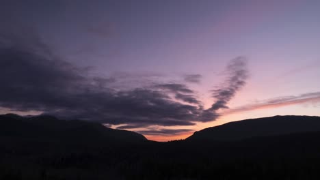 Bei-Sonnenuntergang-Bilden-Sich-Langsam-Wolken-über-Einem-Silhouettierten-Berggebiet,-Hyperlapse-Aus-Der-Luft