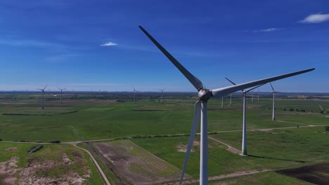 wind turbines spinning on a sunny day in a wide open green field, aerial view