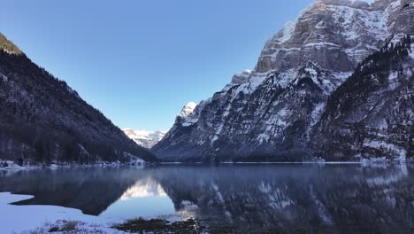 Stunning aerial view of Klöntalersee in Glarus, Switzerland, snow draped mountains mirror in tranquil lake, untouched beauty of winter alps.