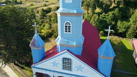 The-iconic-tenaun-church-in-chiloé,-blue-spires-against-green-backdrop,-unesco-site,-aerial-view