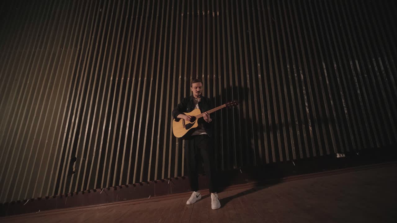 un chico guapo toca una guitarra acústica en un cine abandonado. el músico canta una canción y acompaña en la guitarra
