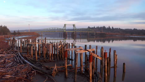 viejos pilotes de madera en la orilla del río con vistas al puente bullards en bandon, oregon
