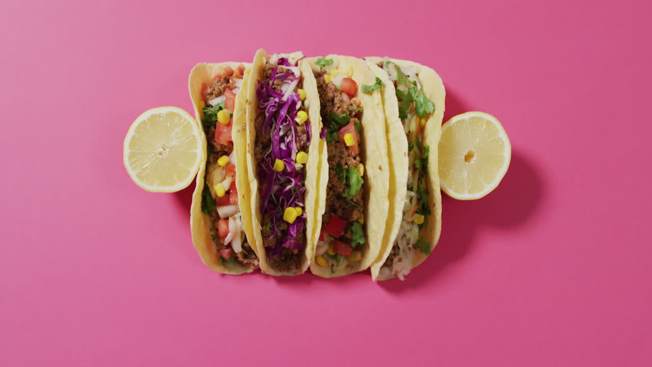 Video af frisk tilberedte tacos liggende på et bræt på lyserød baggrund.