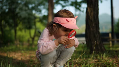 Little-girl-bends-down,-looks-intently-at-dandelion-seeds-with-magnifying-glass