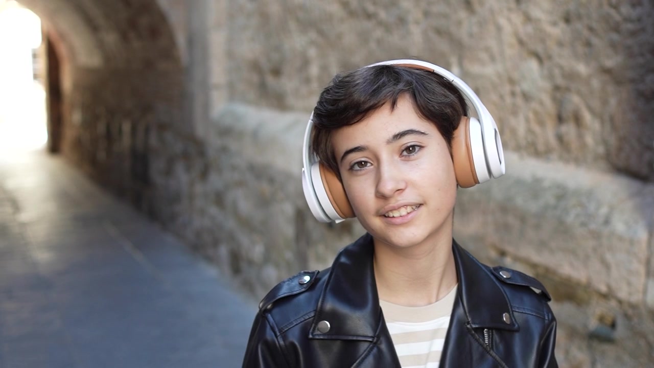 Un giovane ragazzo sorridente con le cuffie in un vivace vicolo urbano, che esprime gioia e divertimento.