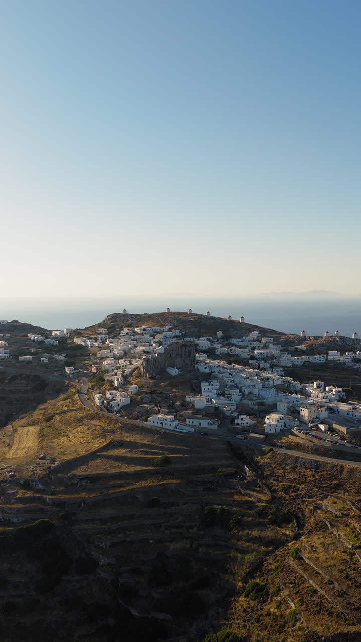 Aerial orbit around the medieval Castle of Amorgos in Chora during sunrise. The iconic Cycladic windmills in the background. Vertical