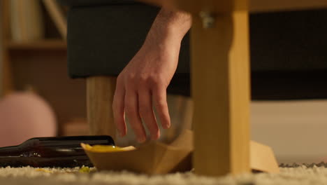 Close-Up-Of-Drunk-Man-On-Sofa-Dropping-Beer-Bottle-Onto-Floor-At-House-Party