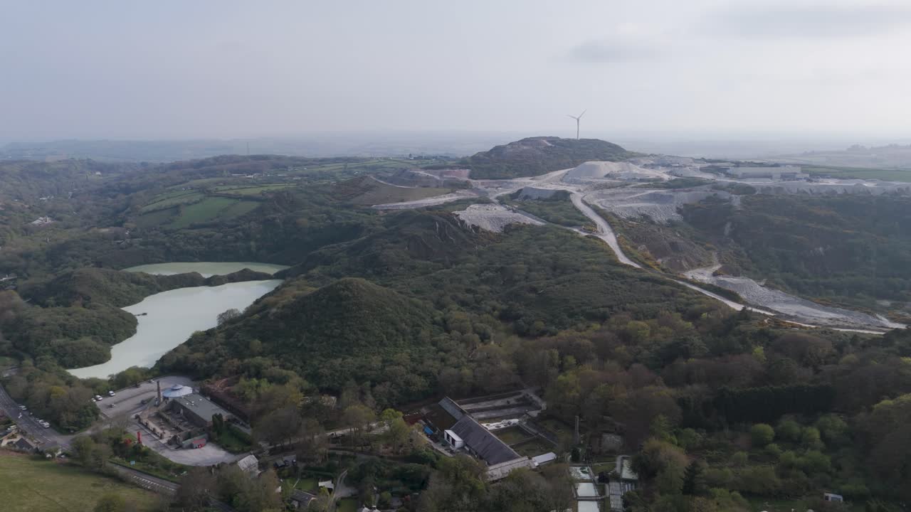 Expansive aerial of active Stenalees aggregate quarry with spiral haul roads, terraces and aquamarine settling lake, illustrating large-scale mineral extraction and landscape transformation