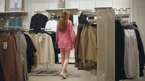 lady dressed in a pink outfit, carrying a black handbag, walks through a neatly arranged, well-lit clothing store, the store features various racks of pants, shirts, and jackets in the store