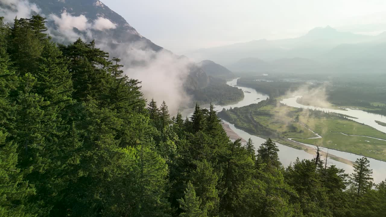 Aerial flyover forest trees of Squamish River and clouds, Squamish, BC, Canada