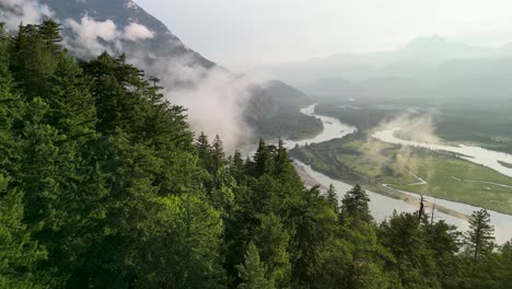 Aerial-flyover-forest-trees-of-Squamish-River-and-clouds,-Squamish,-BC,-Canada