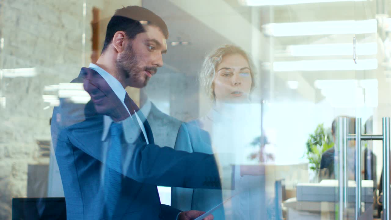 Uomo e donna d'affari discutono il piano di lavoro nell'ufficio di vetro. Persone d'affari indaffarate camminano nel corridoio dell'edificio aziendale