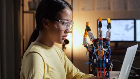 close up of teen asian girl having a backache while working about a cyborg hand on a laptop at home