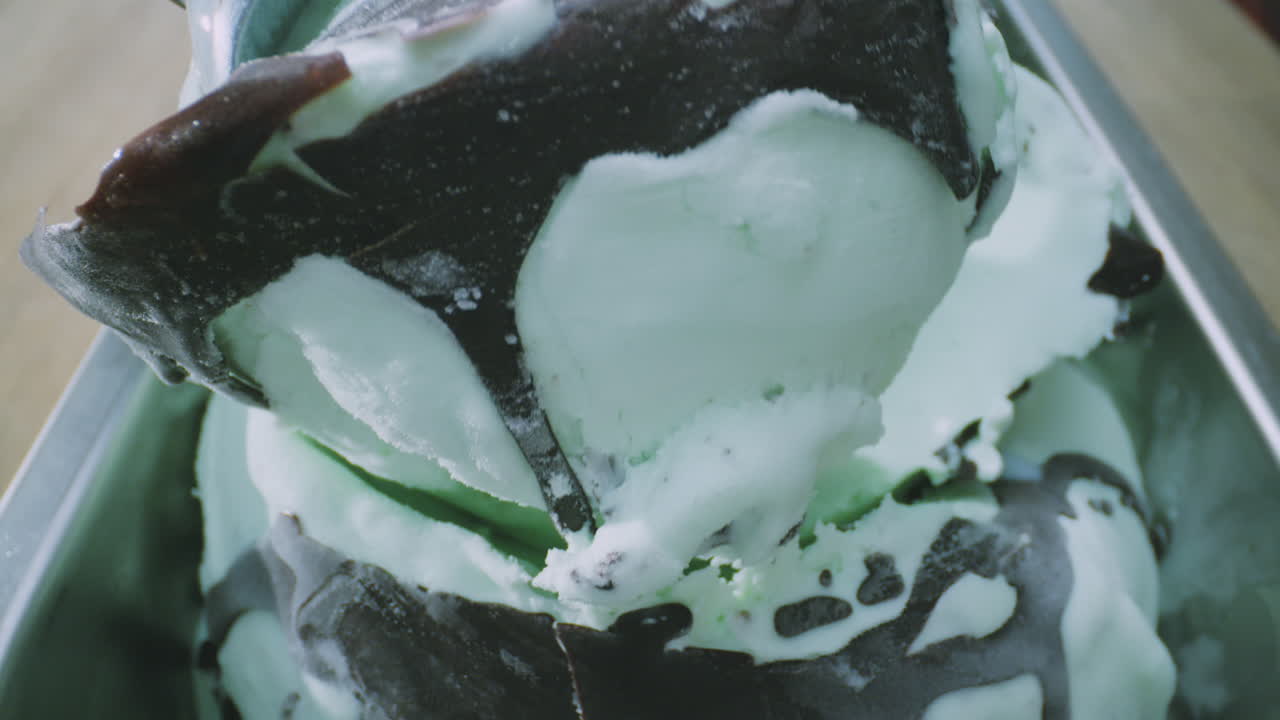 A close-up of a creamy, vibrantly colored mint chocolate ice cream being served with a metal scoop.