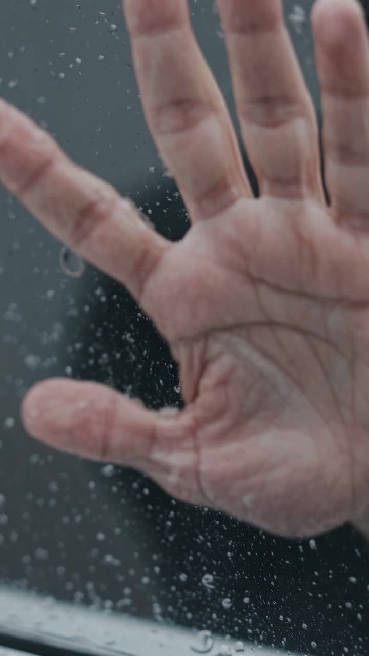 Close-up video shot of a hand pressed against a rain-soaked window, capturing a dramatic