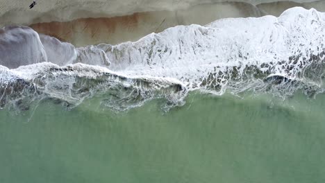 Aerial-view-of-the-beach-on-a-sunny-morning,-with-the-waves-crushing-on-the-sand