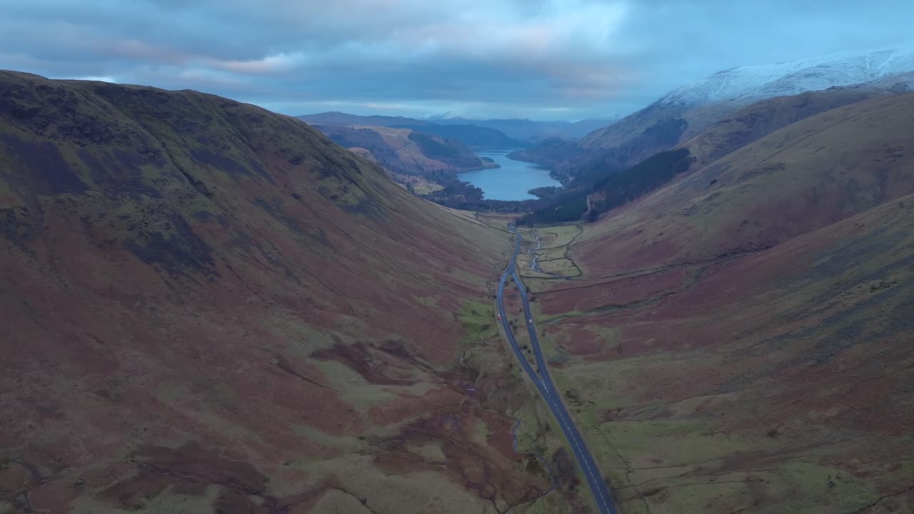 Lateral flight high over mountain pass with lake in the distance. Lake District, Cumbria, UK.