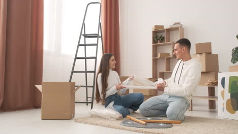 young couple in a new house sitting on the floor unrolling bubble wrap