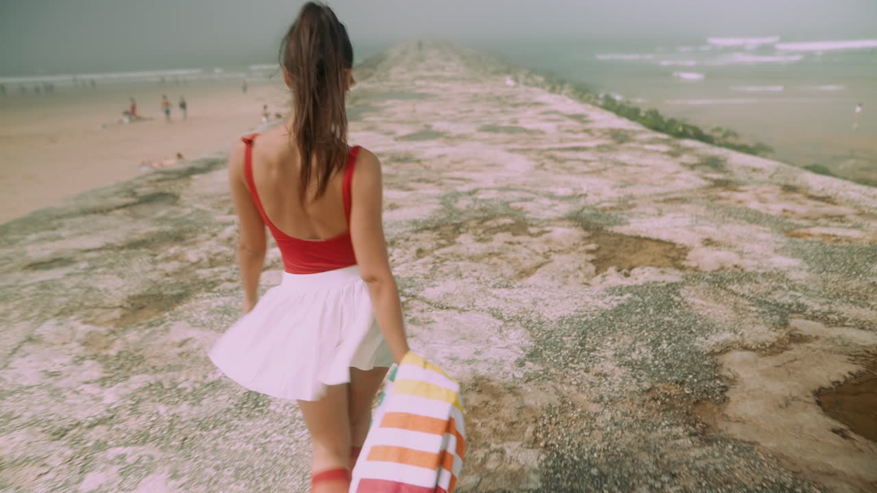 Donna elegante che cammina su un molo verso l'oceano