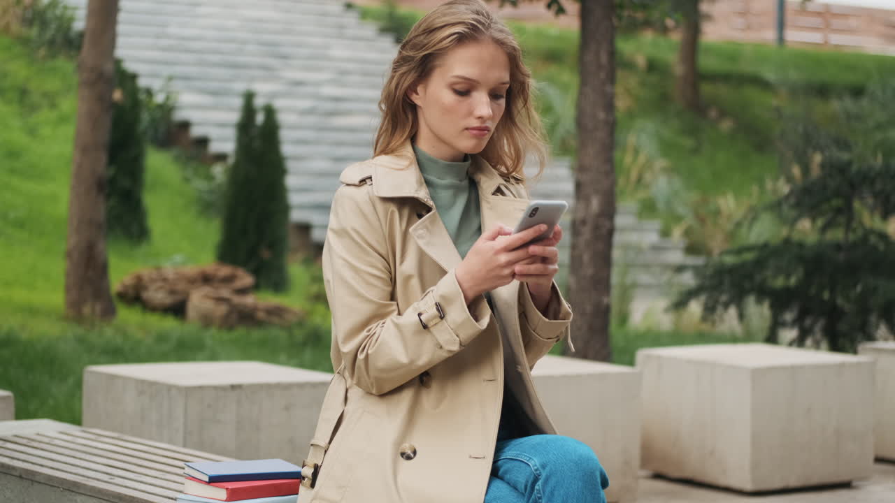 Caucasian female student with smartphone and books at the park.