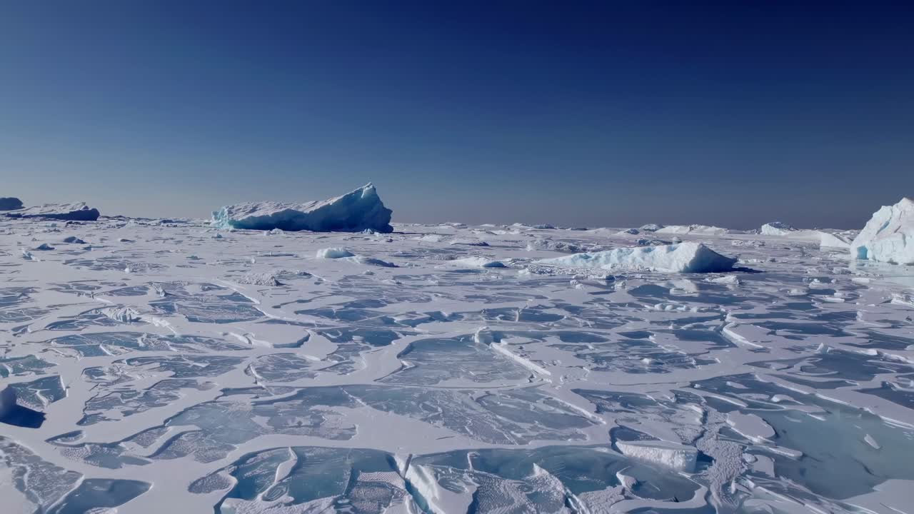 Aerial video captures vast icy landscape with scattered icebergs under a clear blue sky